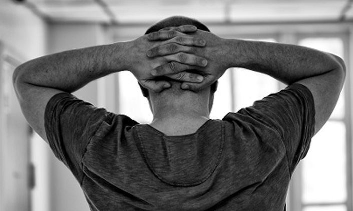 A black and white image of someone gripping the back of their head with both hands.