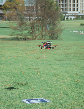 A tethered drone hovering above a marker lying on the University lawn.