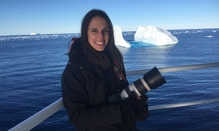 Dr Vanessa Pirotta holding a camera while standing on a boat with sea ice in background