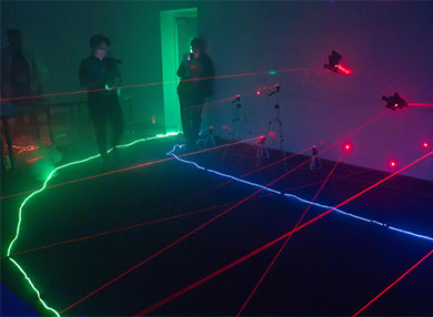 Dark room lit up by neon light strips and red lasers arranged randomly and close together  