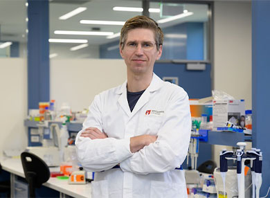 Portrait of Dr Maciej Maselko standing with arms crossed in laboratory