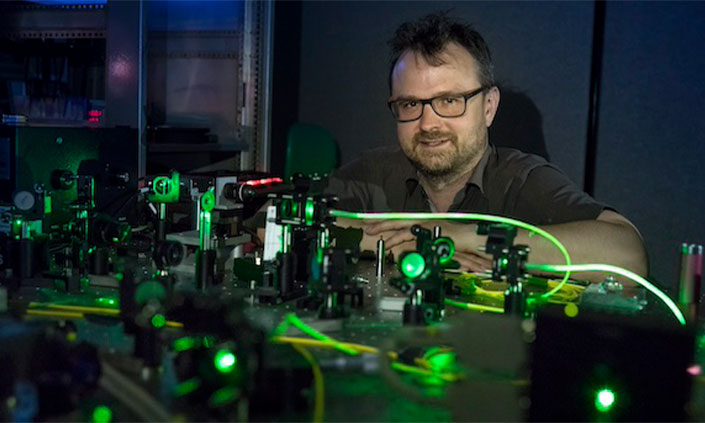 Professor Thomas Volz smiling with quantum optics technology on desk