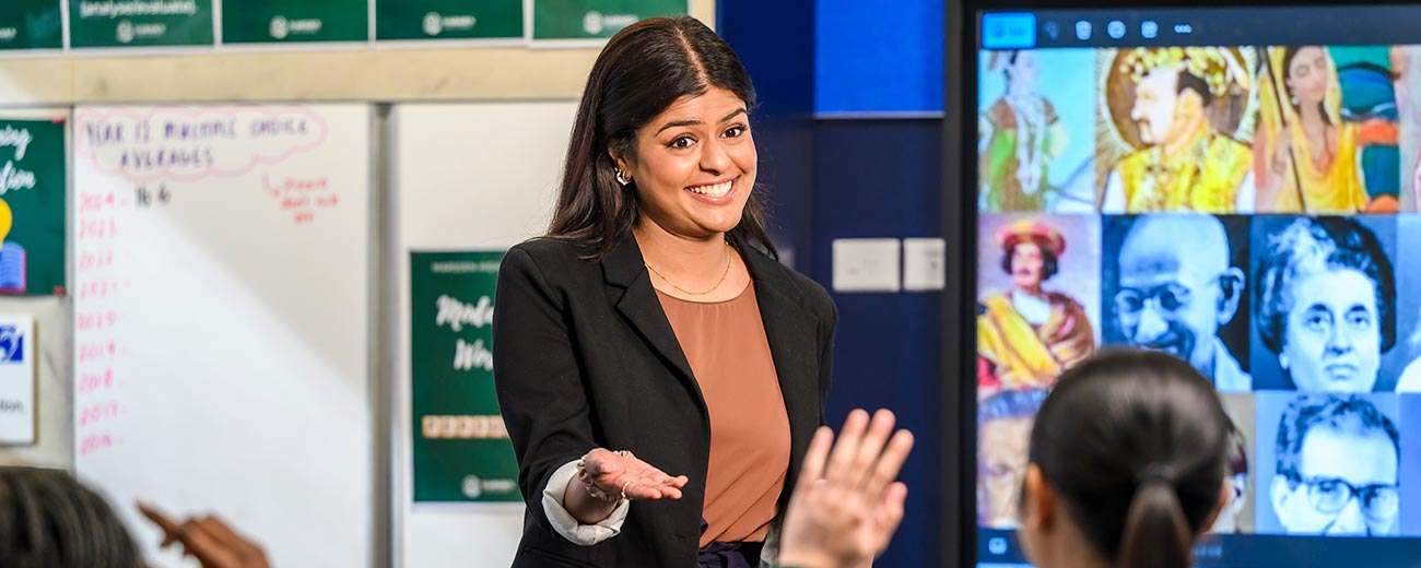 Female teacher in a classroom smiling asking students questions