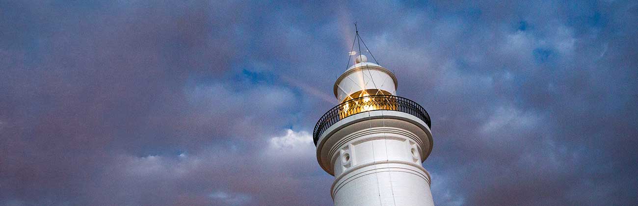 The top of the Macquarie lighthouse, lit up against a stormy sky.