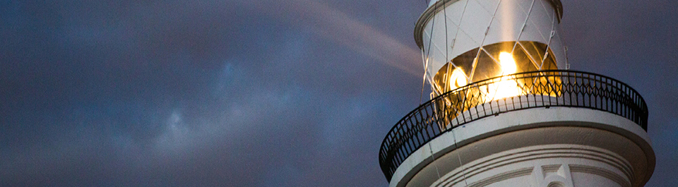 The top of the Macquarie lighthouse, lit up against a stormy sky.