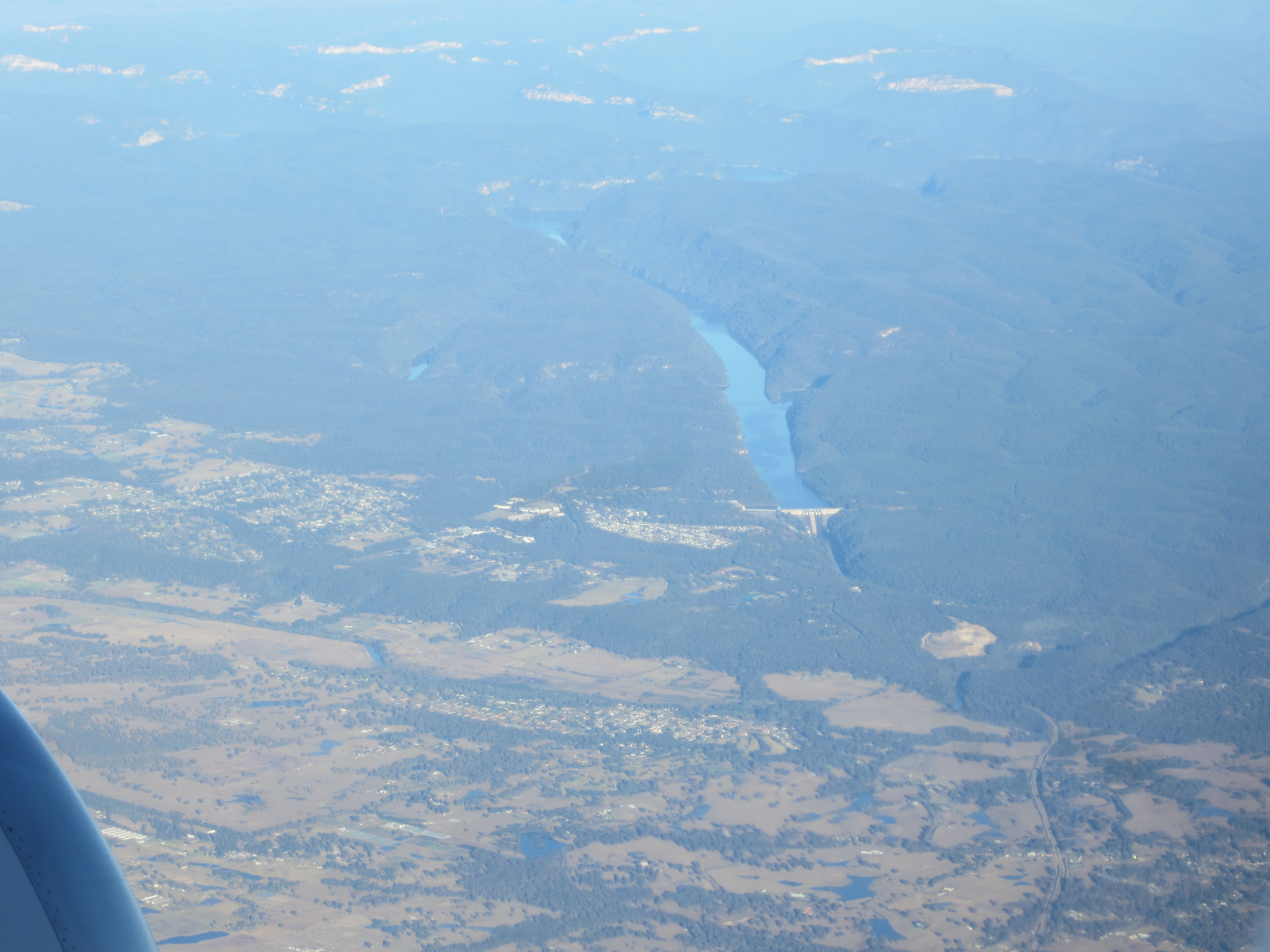 An aerial photograph taken from a plane of  a river and dam. There are two towns below the dam which can be seen in the image