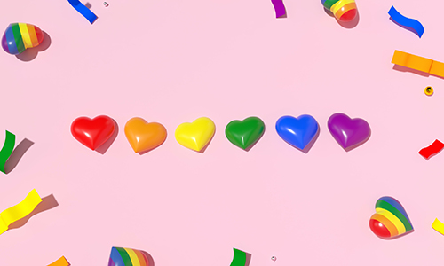 Six heart decorations in rainbow colours, surrounded by colourful confetti.