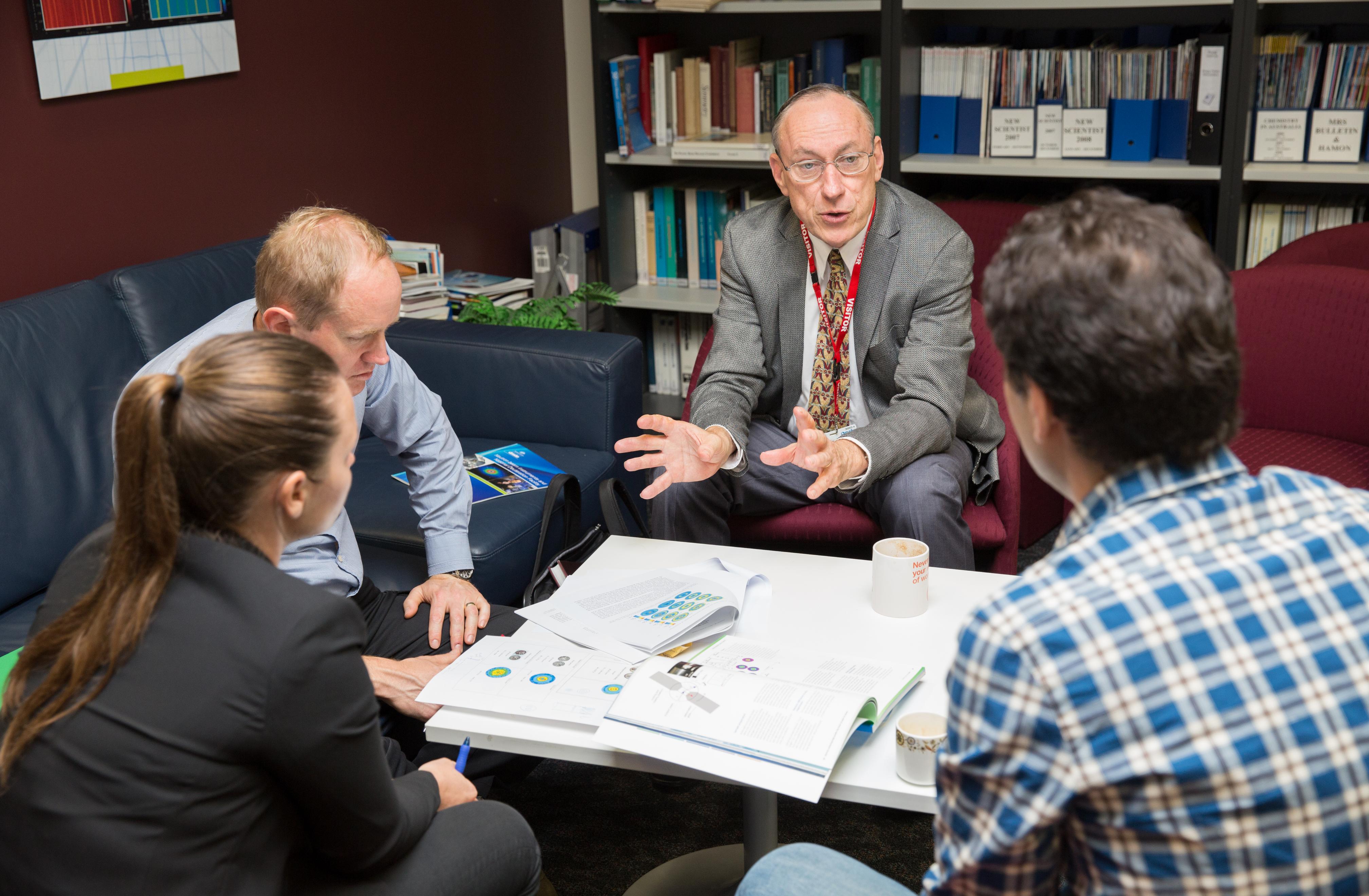 Five people having discussion around a table with paper on it. 