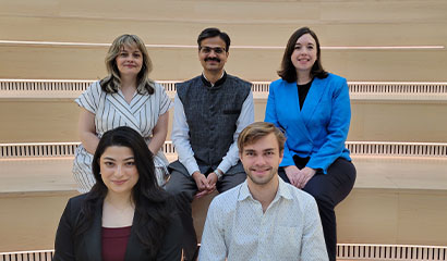 Five people in semi-formal clothing sitting on stairs and smiling at the camera.