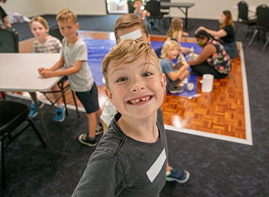 A group of kids playing in a room, with one child looking and smiling at the camera.