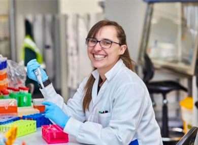 Image of Dr Paige Erpf  smiling in a lab-coat and working in a laboratory 