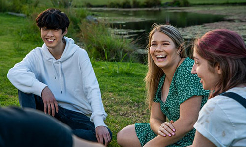 Students sitting on the lawn by the lake.