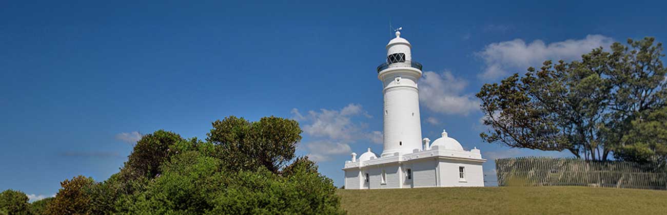 White lighthouse perched on top of a grassy hill encircled by blue skies.