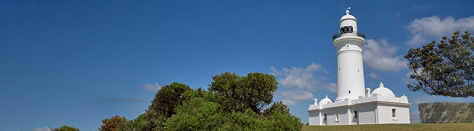 White lighthouse perched on top of a grassy hill encircled by blue skies.
