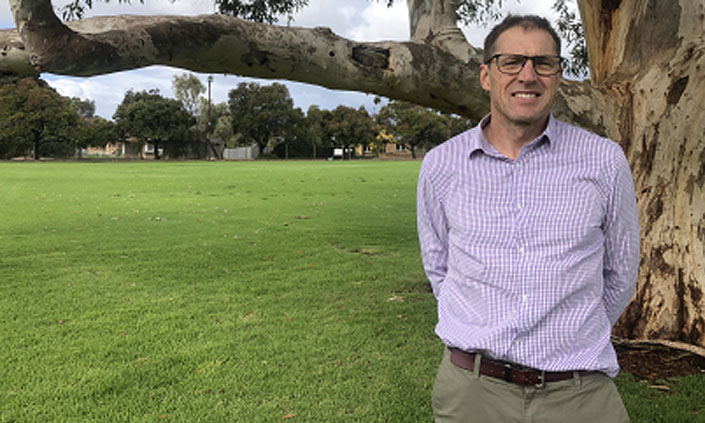 A person standing outside by a tree wearing glasses and a button-up shirt.