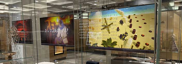 Overview image of museum display featuring video game 'Save One More' and trench art objects