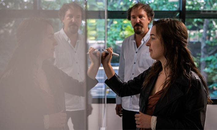 Two researchers standing at whiteboard with one holding a blue marker up to the board