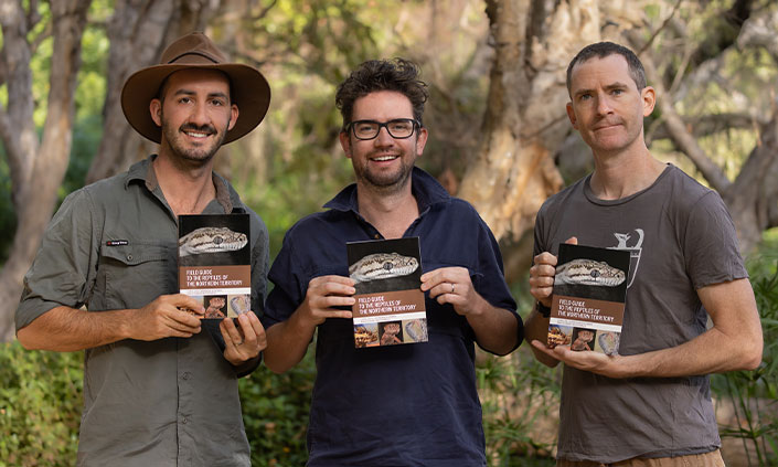 Dr Jolly and his friends and co-authors Brendan Schembri and Dr Stewart Macdonald posing while holding their book with nature behind