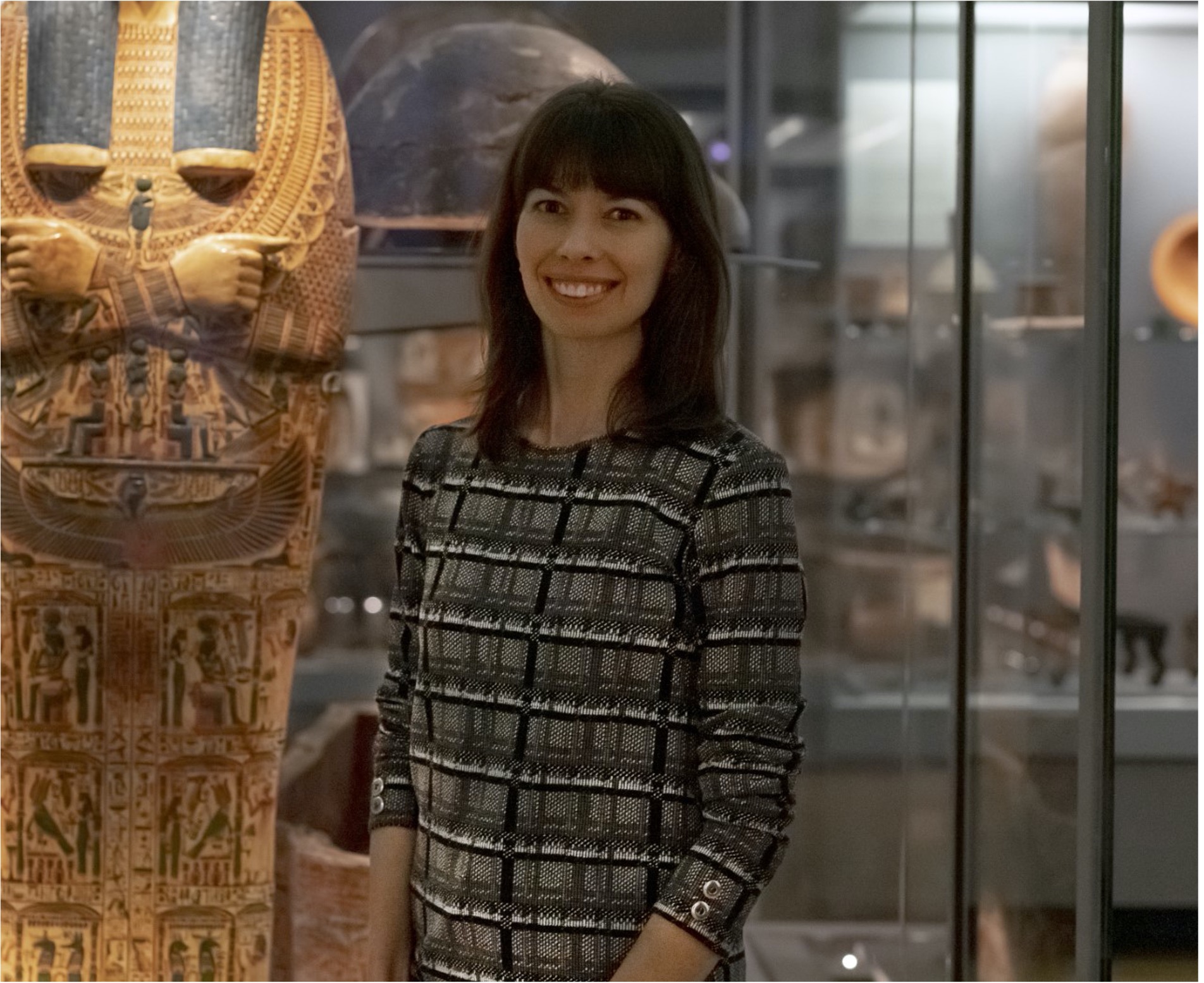 A woman smiling at the camera in front of a museum display of ancient Egyptian antiquities 