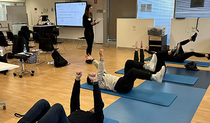 A GLAD Back instructor supervises four patients lying on yoga mats on the floor, on their backs with their limbs in the air.