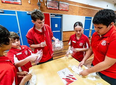 Five children in school uniforms doing a science experiment with plastic bags.