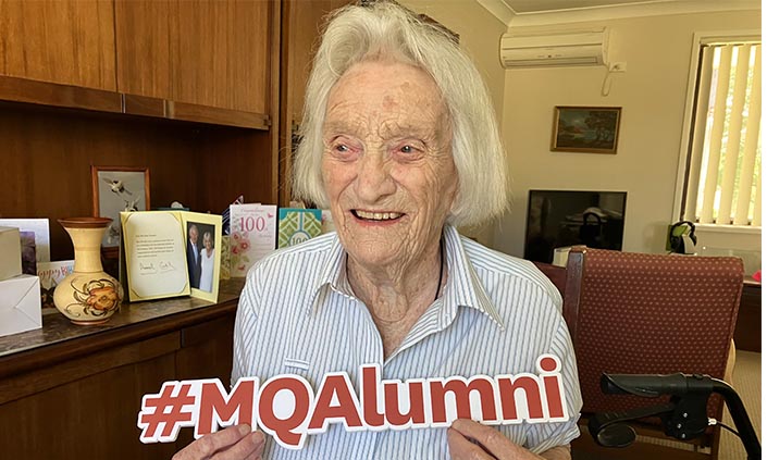 Image of Betty holding up a sign that reads #MQAlumni