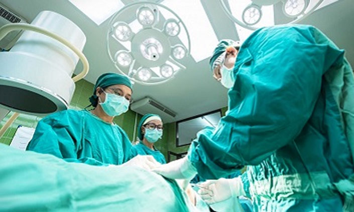 Three medical professionals wearing scrubs in an operating room.