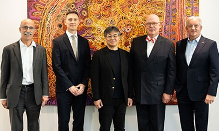 Five executives and professionals in suits smiling at the camera at an event.