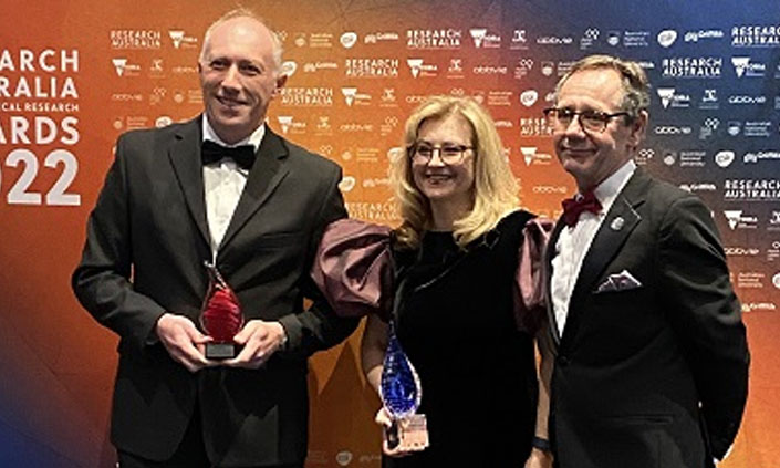 Three people in dress attire holding an award and smiling at the camera.