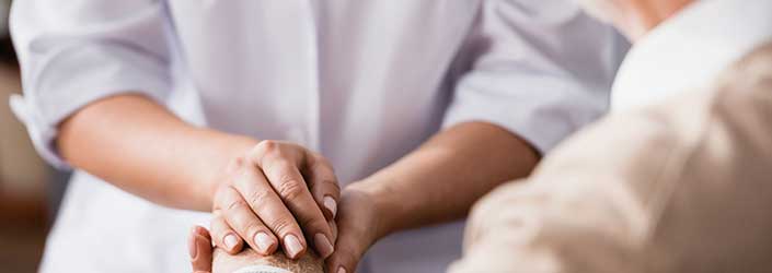 A person wearing scrubs holding the hand of an elderly person.