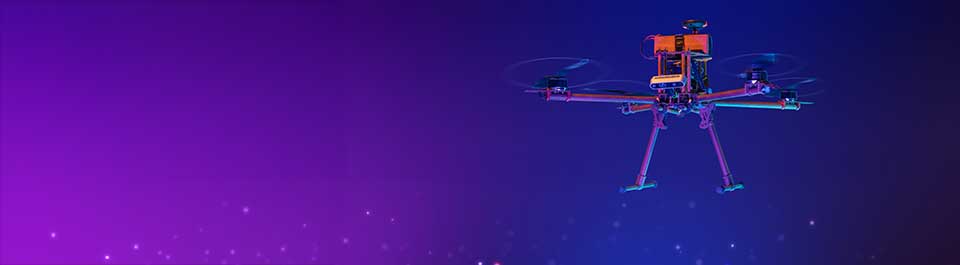 A drone in flight, lit with orange light against a dark background.