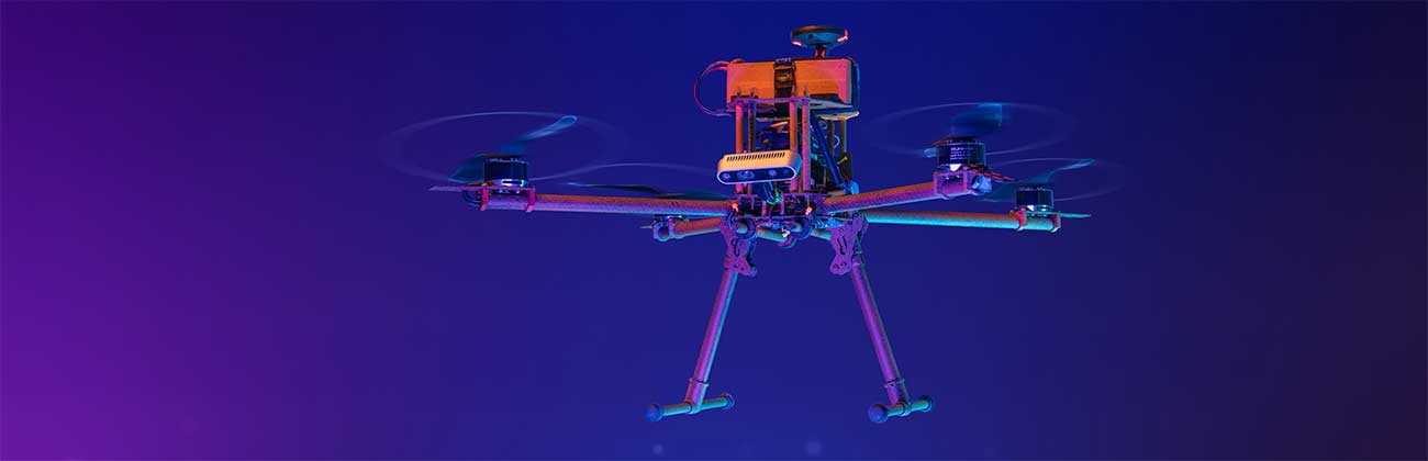 A drone in flight, lit with orange light against a dark background.
