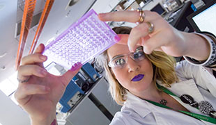 Lady with safety goggles and lab gown doing an experiment