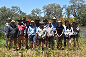 Group of people standing in bushland with waterway and trees in background 
