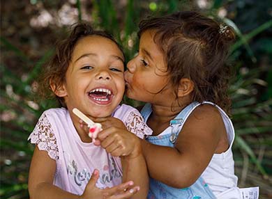 Two children sitting at a table, with one child kissing the other on the cheek.