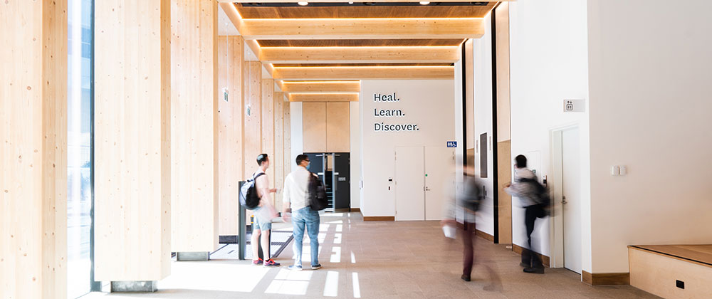 Students walking in the faculty building foyer, with a sign that says Heal. Learn. Discover.