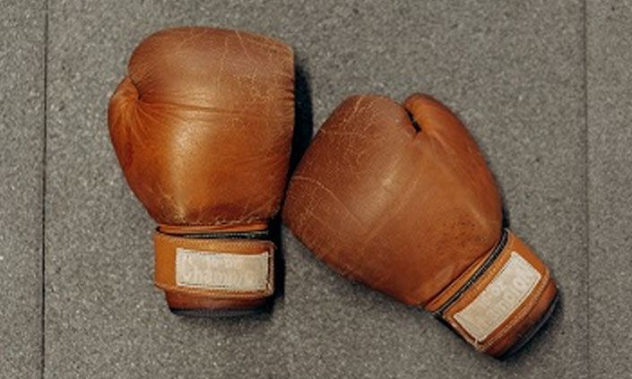 Two brown boxing gloves laying flat on the ground.