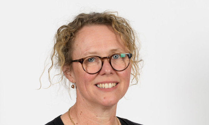A headshot of a professional wearing glasses and smiling at the camera.