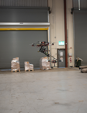 Two drones flying inside a warehouse, transferring cargo between them.