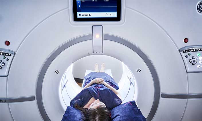 A woman lying on a bed going into an MRI machine