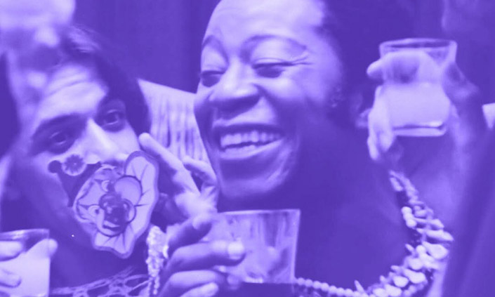 A still from a Brazilian film, in blue-toned monochrome. Smiling people hold glasses of cloudy liquid.
