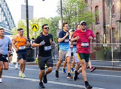 A group of people running down a Sydney street with the Harbour Bridge behind them