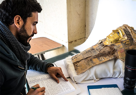 Dr Carlo Rindi Nuzzolo writing notes while examining ancient Egyptian mummy mask