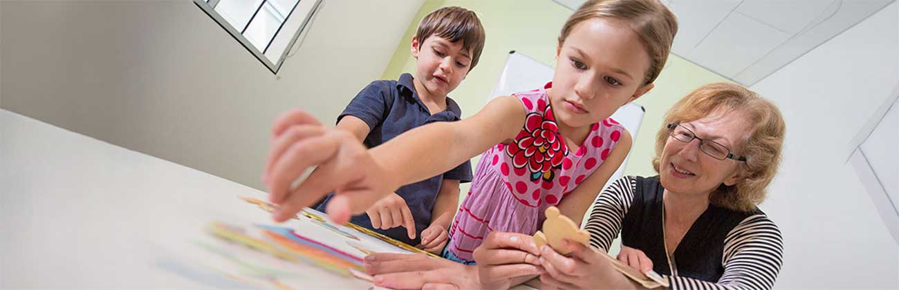 A clinician watching two children play with a puzzle