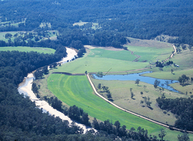An aerial view of the Tuross River, winding between dark green forests and lighter green fields.