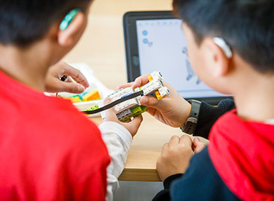 Two children wearing hearing aids, playing with Lego