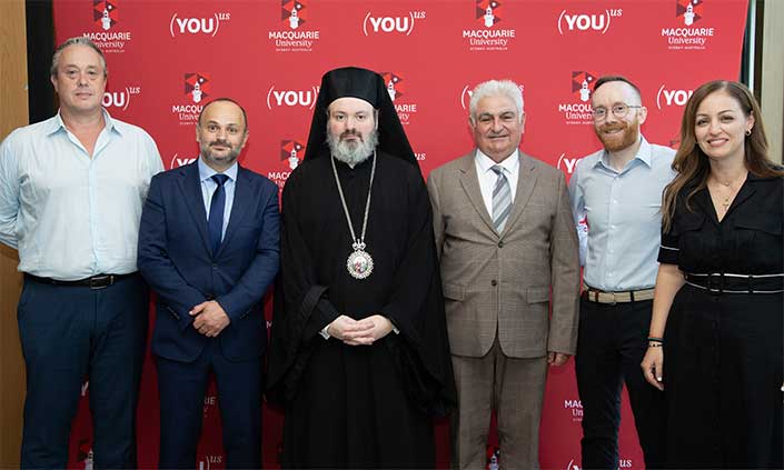 Six people standing in front of a Macquarie University banner