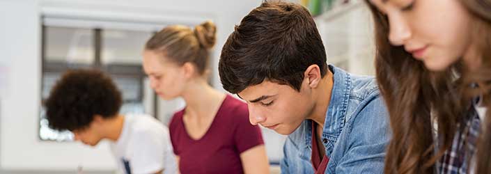 A student in a busy classroom writing in a notebook.