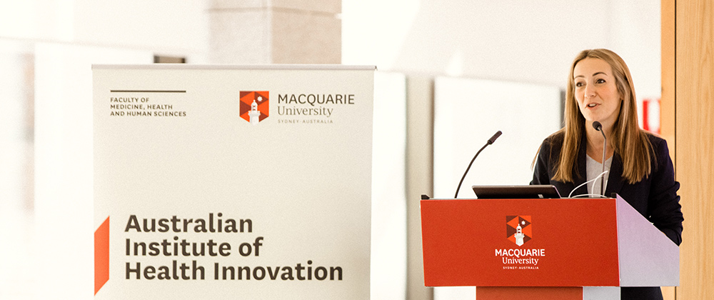 A speaker at a podium, standing next to a banner that reads Australian Institute of Health Innovation.