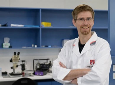Portrait of Dr Maciej Maselko in a lab-coat inside lab
